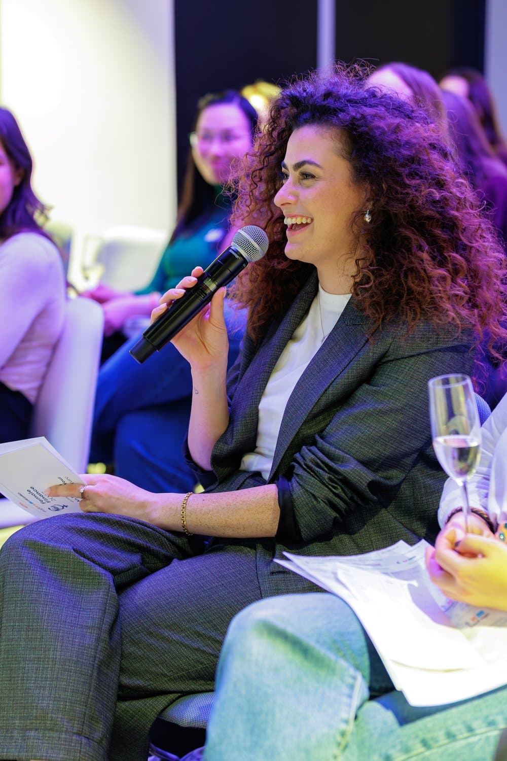 נועם יוסף יושבת עם מיקרופון, צוחקת, בערב Women in Finance